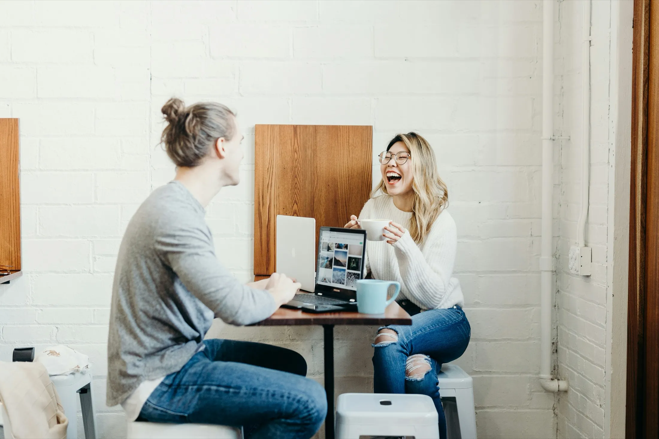 Two colleagues laughing at a shared laptop